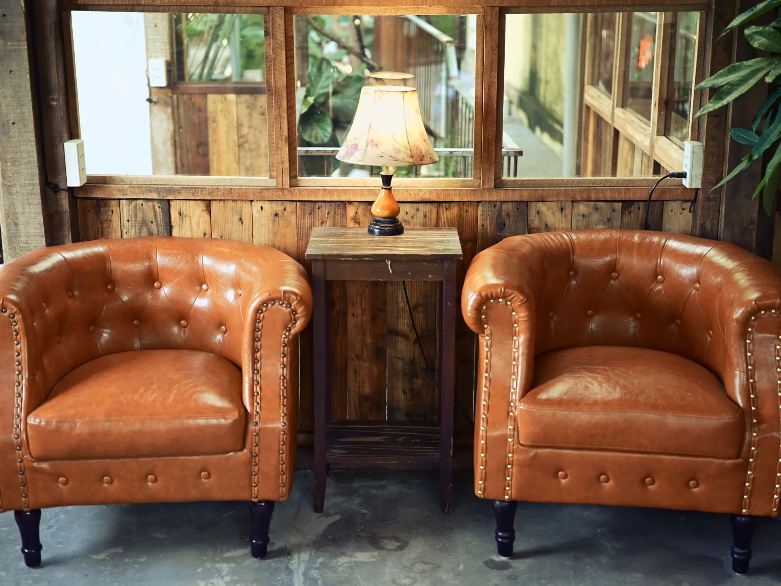 Coin salon chiné avec deux fauteuils club en cuir capitonné, guéridon en bois et lampe ancienne